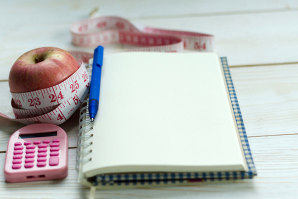 health and body slimming fitness concept. opened notebook, pen, red apples, calculator and measuring tape on white wooden table